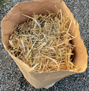 Paper bag of barley straw
Open brown paper bag filled with golden barley straw, viewed from above on a gravel surface.