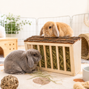A light wood rabbit hay feeder filled with green hay, with two rabbits—a fluffy gray one eating hay in the foreground and a tan one sitting on top of the feeder in the background.