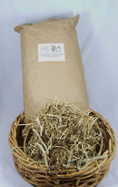 Paper sack of English Timothy hay behind a wicker basket filled with loose hay.